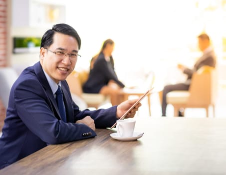 Portrait of Businessman working in cafe with smart phone and tablet with business team in background using for coporate background work