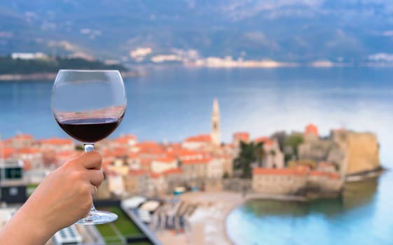 Woman holding glass with red wine on the balcony of her apartment in the Budva town, Montenegro