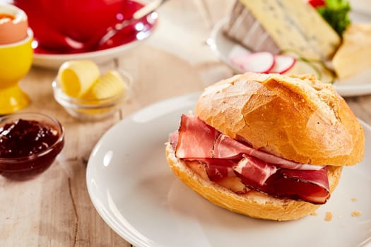 Slices of crispy bacon in fresh white bread bun, served on ceramic plate in restaurant. Viewed in close-up, with butter, cheese and ketchup in background