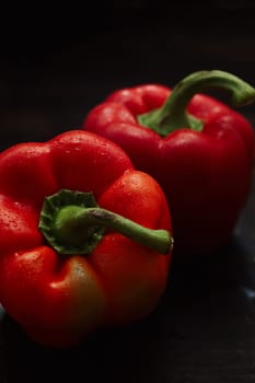 Two wet washed raw fresh red bell peppers or capsicum with green stalks for a healthy salad ingredient on a shadowy dark background viewed high angle close up