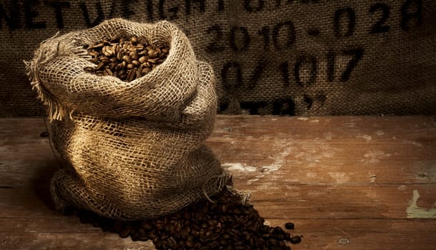 Fresh roasted coffee beans in a hessian sack on a rustic wood floor with hessian background with stencilled text and copy space for product placement