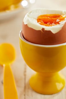 Close-up on open soft-boiled organic egg in yellow ceramic eggcup served with plastic spoon