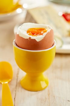 Soft-boiled egg served in yellow ceramic eggcup on wooden table with plastic spoon