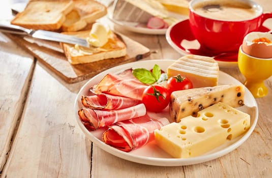 Variety of cheese and bacon served for sandwiches on white plate, with fresh tomatoes, toasts, boiled egg and cup of coffee
