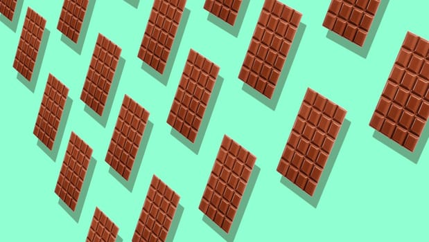 Pattern of many whole milk chocolate tablets with shadows on cyan background, viewed in perspective and full frame