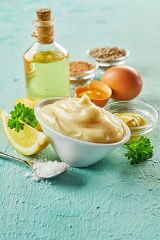 Ingredients for making gourmet homemade mayonnaise with eggs, lemon, oil and spices on textured green wood with foreground copy space