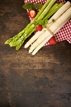 Two bundles of fresh raw green and white asparagus spears tied with string on a checked red and white cloth on rustic wood with copy space