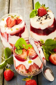 Assorted individual strawberry desserts with creamy mousse and berry coulis topped with nuts and candy pearls on a rustic wooden table
