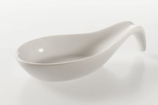 Clean empty white ceramic spoon for food presentation and styling diagonally on a white background with reflection