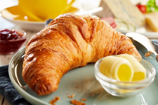 Whole fresh baked flaky croissant served with butter curls. Close-up view