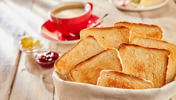 Fresh white bread toasts for breakfast, served in fabric bag with butter, jam and cup of coffee blurred in background