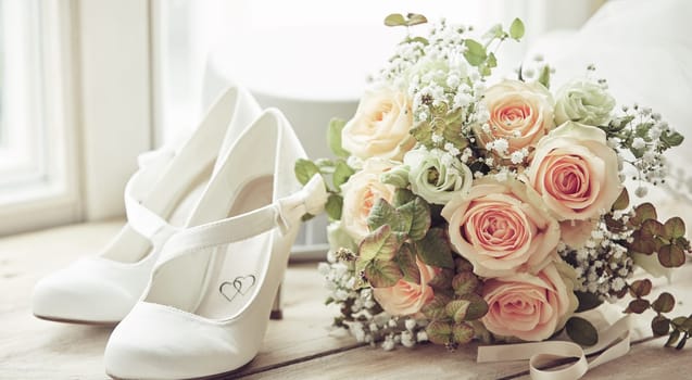 Bridal bouquet, pair of white shoes decorated with hearts and white hat. Wedding composition sitting on window sill in bright light, viewed in close-up