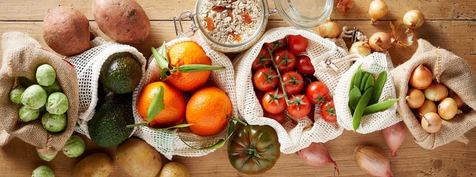 Fresh organic vegetables assortment viewed from above on wooden background, packed in reusable eco-friendly fabric bags. Groceries from local market banner concept
