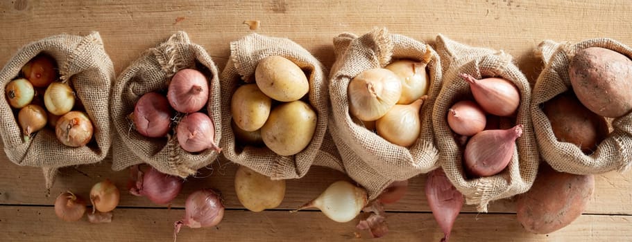 Top view of onion assortment and potatoes in sack bags in rustic farm harvest of organic vegetables concept banner
