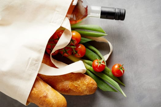 Fresh groceries and wine in a reusable fabric shopping bag to replace polluting plastics over a slate background with copy space