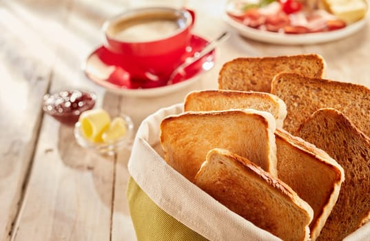 Freshly made crunchy toasts, served in fabric bag with coffee and butter blurred in background on wooden table