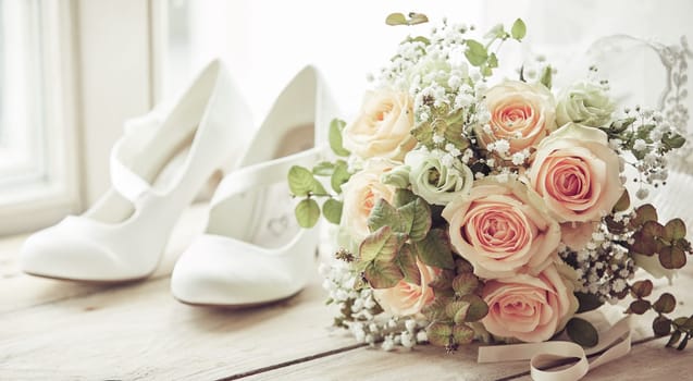 Brides white shoes and beautiful wedding bridal bouquet of pink roses in close-up on wooden sill of bright window