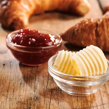 Butter curls and jam as filling for croissants, served in small glass bowls on scratched wooden table. Close-up side view