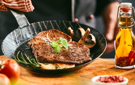 Seasoned portion of grilled beef steak with herbs and mushroom presented in an old vintage black skillet or pan