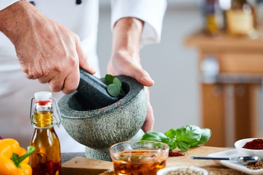 Chef crushing a blending fresh herbs in a stone pestle and mortar in a close up view on his hands