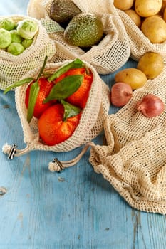 Assortment of organic groceries in reusable eco-friendly net bags. Fresh oranges, avocados, Brussels sprouts, potatoes and onion on blue wooden table, viewed from above in close-up