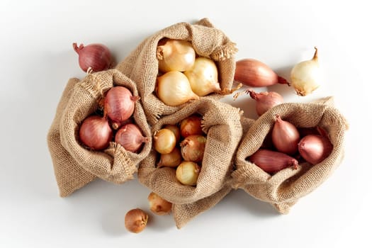 Burlap sack bags with various onions from local market, viewed from above and isolated on white background with shadow