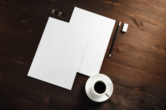 Blank letterheads, coffee cup, pencil and eraser on wood table background. Responsive design template. Flat lay.