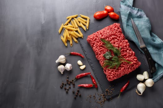 Still life with fresh forcemeat from beef, vegetables, pasta and spices on a dark background. Top view with copy space