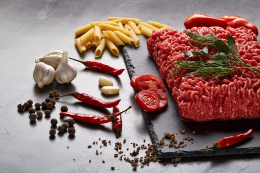 Still life with fresh forcemeat from beef, vegetables, pasta and spices on a dark background.