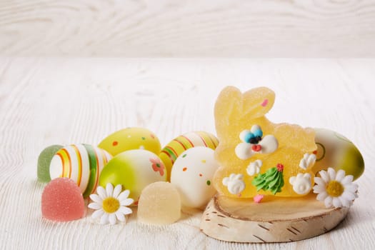 Still life with colored easter eggs and easter rabbit from sweet fruit jelly on a light wooden background. Greeting card.