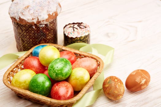 Still life with colored easter eggs and easter cakes lying on a wooden table on light background. Greeting card. Selective focus on eggs
