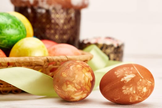 Still life with colored easter eggs and easter cakes lying on a wooden table on light background. Greeting card. Selective focus on eggs