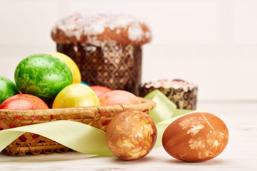 Still life with colored easter eggs and easter cakes lying on a wooden table on light background. Greeting card. Selective focus on eggs