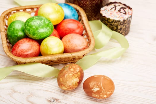 Still life with colored easter eggs and easter cakes lying on a wooden table on light background. Greeting card. Selective focus on eggs