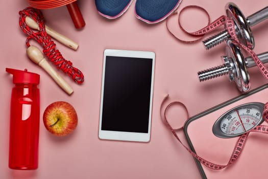 Female fitness still life. Sport accessories, scales, computer tablet on pink background. Mockup. Planning of diet and trainings. Top view, copy space. Healthy lifestyle concept. Slimming