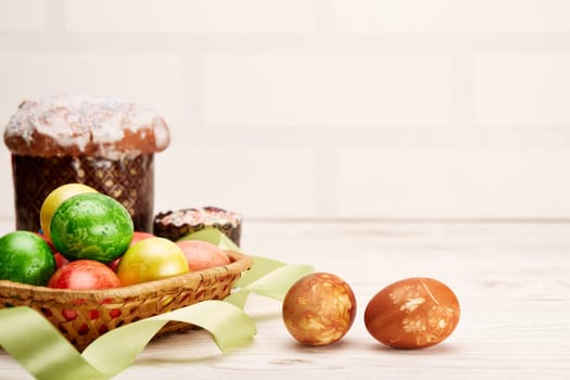 Still life with colored easter eggs and easter cakes lying on a wooden table on light background with copy space. Greeting card. Selective focus on eggs
