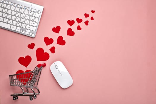 Shopping trolley, Computer keyboard and mouse, decorative red hearts on pink background with copy space. Concept of internet shopping. Valentine's day, Mother's day, wedding