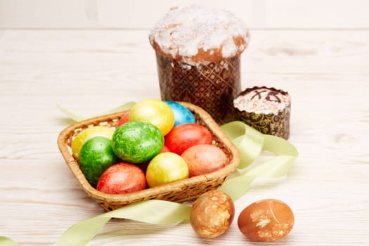 Still life with colored easter eggs and easter cakes lying on a wooden table on light background with copy space. Greeting card. Selective focus on eggs