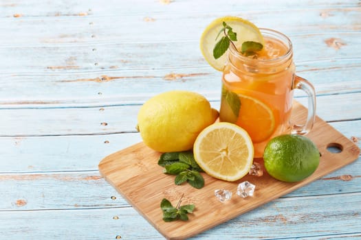 Citrus lemonade with ice, leaves of mint, lemon and lime slices standing on blue wooden table. Homemade lemonade with citruses. Healthy cool beverage