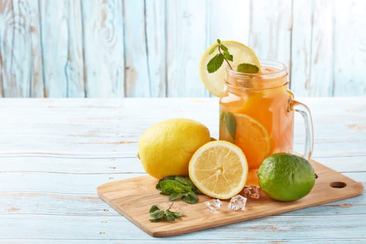 Citrus lemonade with ice, leaves of mint, lemon and lime slices standing on blue wooden table. Homemade lemonade with citruses. Healthy cool beverage