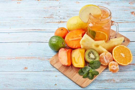 Fruit lemonade with ice, leaves of mint, lemon, pineapple, mango and lime slices standing on blue wooden table. Homemade lemonade with mix fruits. Healthy cool beverage, fruit juice. Top view