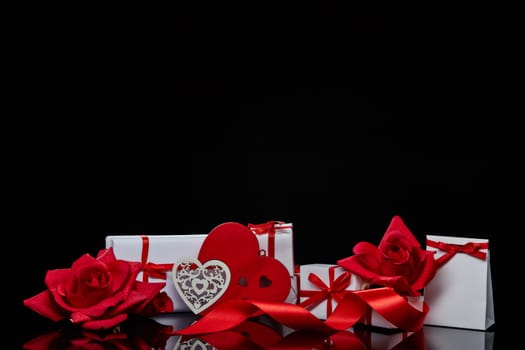 Gift boxes and red roses and decorative heart on black background. Valentine's Day card with copy space. Design element for romantic greeting card, wedding invitation