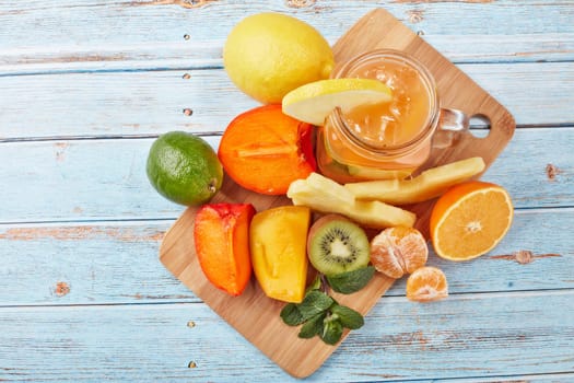 Fruit lemonade with ice, leaves of mint, lemon, pineapple, mango and lime slices standing on blue wooden table. Homemade lemonade with mix fruits. Healthy cool beverage, fruit juice. Top view