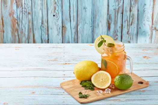 Citrus lemonade with ice, leaves of mint, lemon and lime slices standing on blue wooden table. Homemade lemonade with citruses. Healthy cool beverage