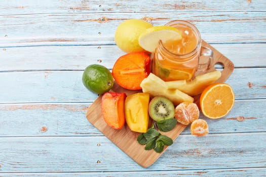 Fruit lemonade with ice, leaves of mint, lemon, pineapple, mango and lime slices standing on blue wooden table. Homemade lemonade with mix fruits. Healthy cool beverage, fruit juice. Top view