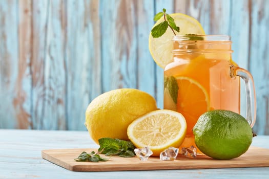 Citrus lemonade with ice, leaves of mint, lemon and lime slices standing on blue wooden table. Homemade lemonade with citruses. Healthy cool beverage