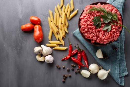Still life with fresh forcemeat from beef in a bowl, vegetables, pasta and spices on a dark background. Top view