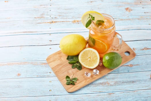 Citrus lemonade with ice, leaves of mint, lemon and lime slices standing on blue wooden table. Homemade lemonade with citruses. Healthy cool beverage