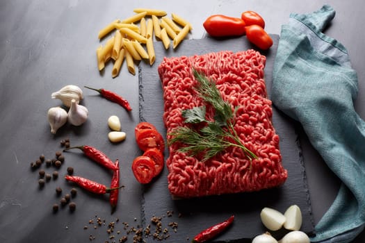 Still life with fresh forcemeat from beef, vegetables, pasta and spices on a dark background. Top view