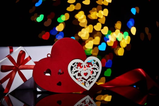 Gift boxes and decorative hearts on a black background with heart-shaped bokeh . Valentine's Day card with copy space. Design element for romantic greeting card, wedding invitation